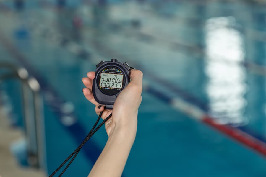 coach holding up stopwatch poolside